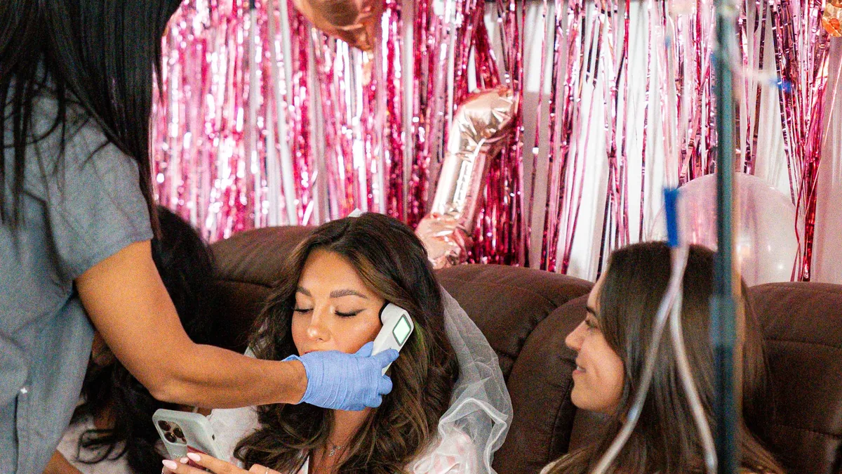 A Drip Lab nurse checks on a bride in her veil and her friends on the couch